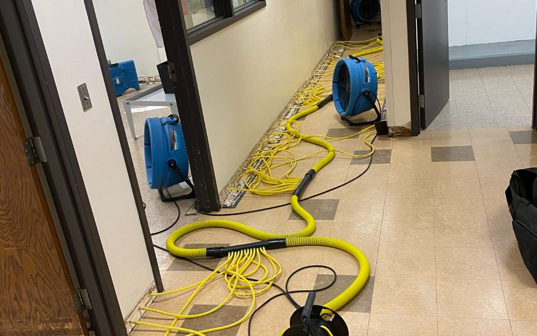Air movers and wall-cavity drying hoses in a commercial hallway