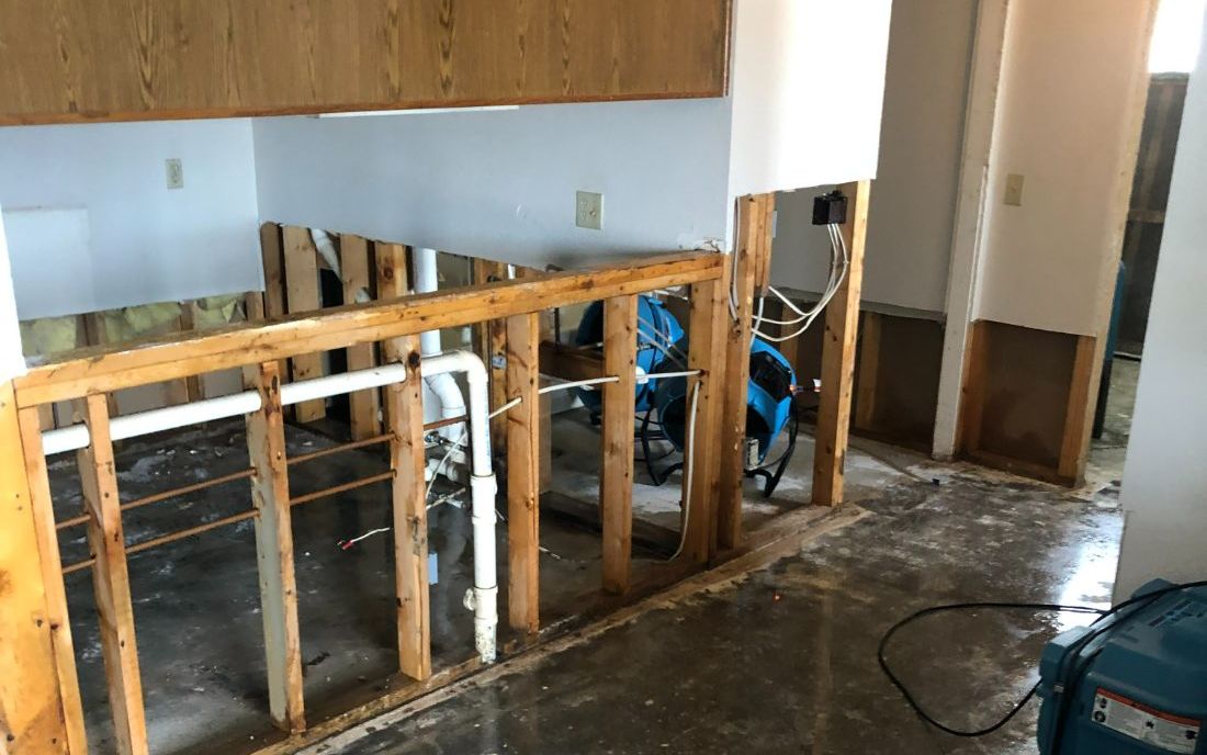 Water-damaged kitchen with wet floor, opened walls and drying equipment
